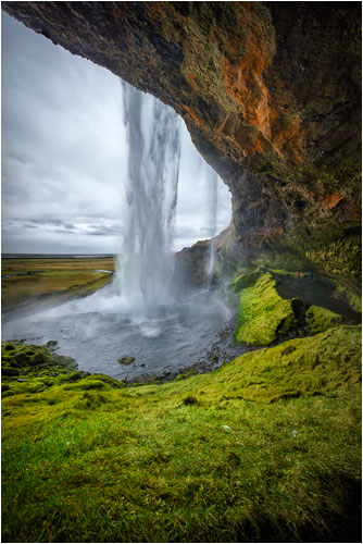 Hinter der Kulisse vom Seljalandsfoss. Mitte-rechts vom Bild sind zwei Menschen zu sehen. 